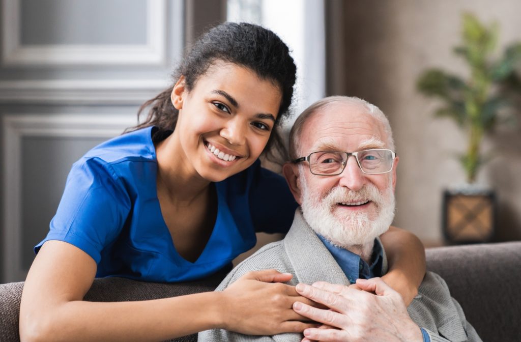 A caregiver behind a senior man putting her arms around him in a memory care community