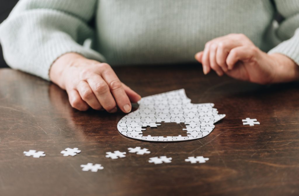 An older woman completing a puzzle that looks like a head, with pieces missing from the brain
