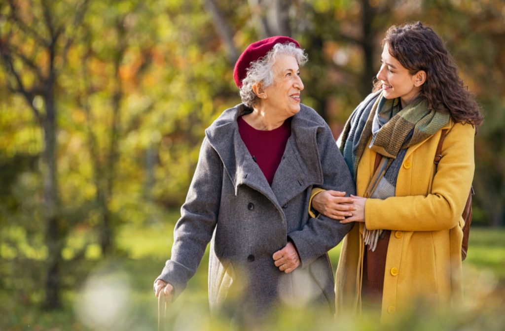 a woman walks with a senior woman with memory loss in a park having a conversation
