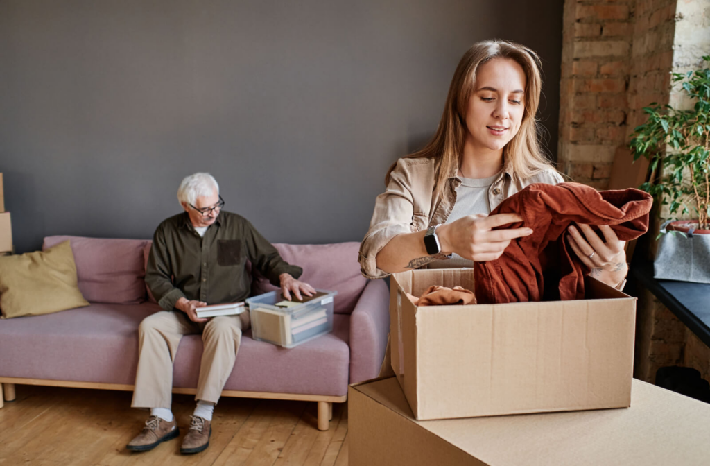 A young woman helping a senior man pack his belongings into a cardboard box.