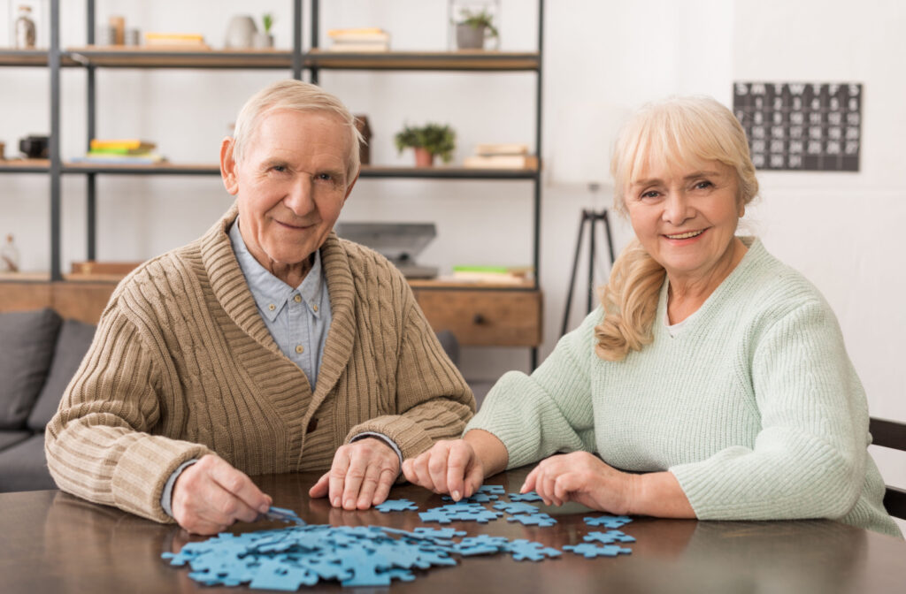 A senior couple in cozy sweaters solving a jigsaw puzzle on a wooden table.