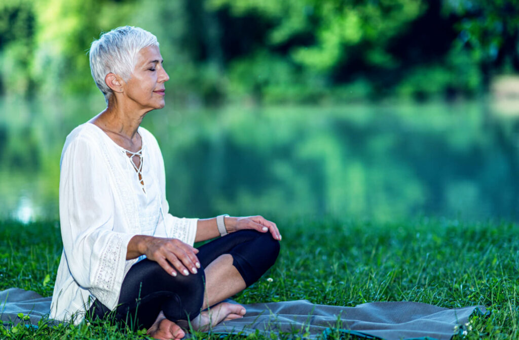 A mindful short-haired woman meditating beside a body of water.
