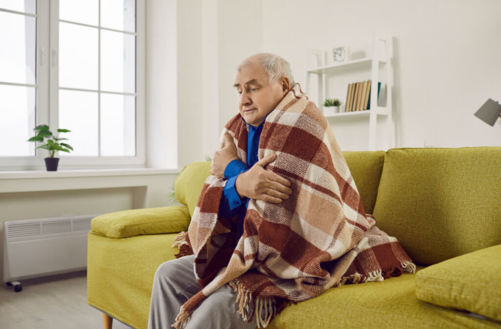 An older man trying to keep warm under a blanket.