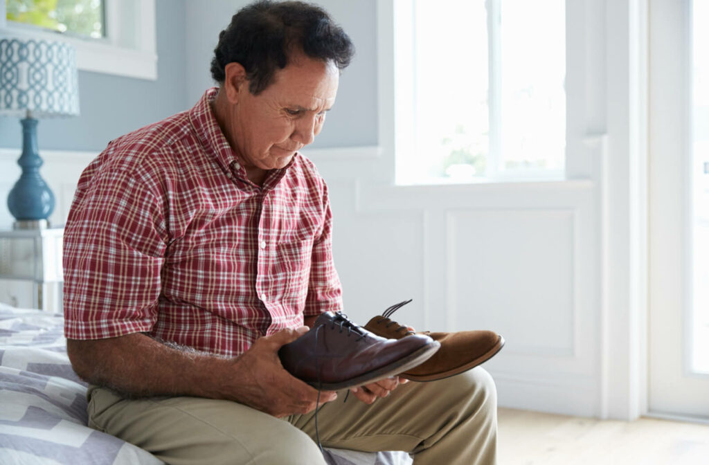 An older adult man sitting on a bed and choosing what shoes to wear