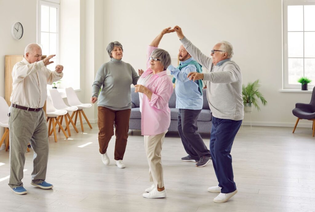 Five seniors practice dance moves they learned in a class while in a clean, open room in their retirement community