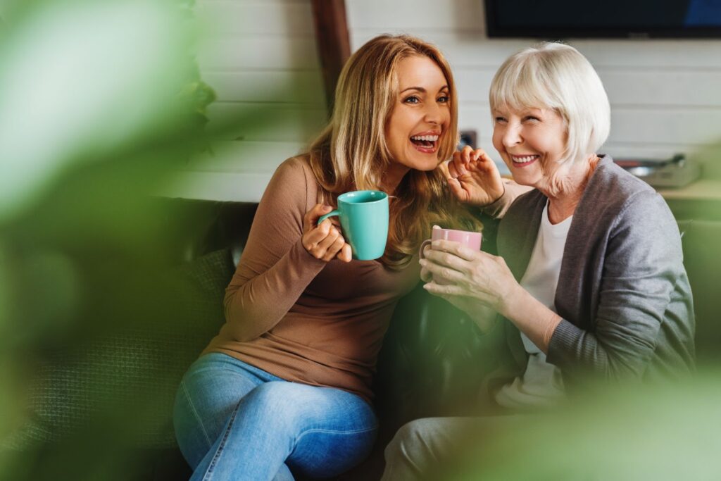 A smiling senior visits with her adult daughter as they share a cup of tea.