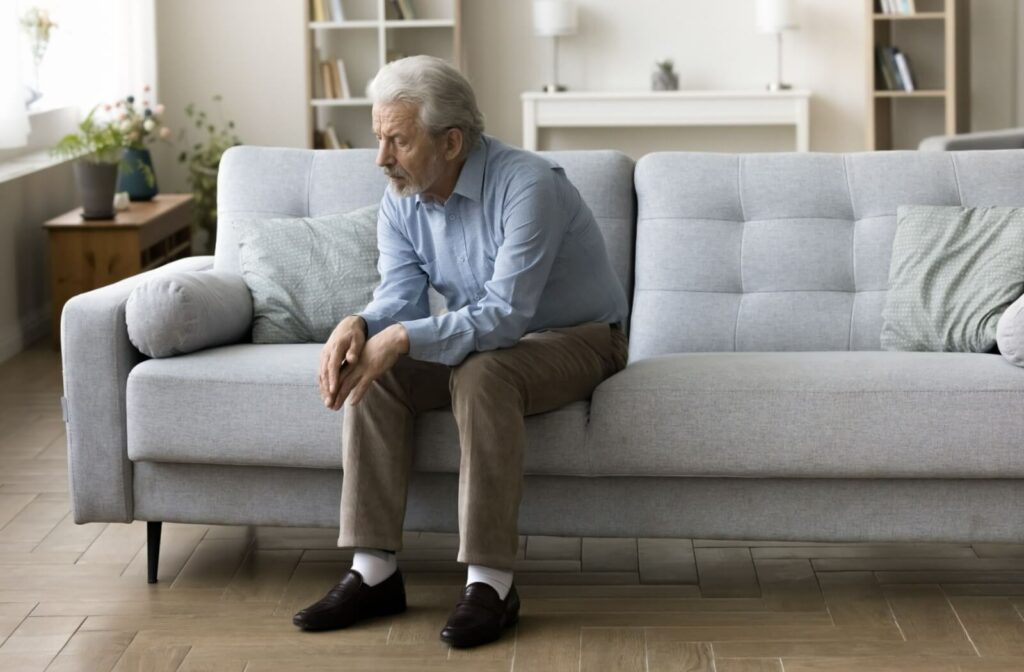 A senior struggling with memory loss sitting alone on the couch looking frustrated.